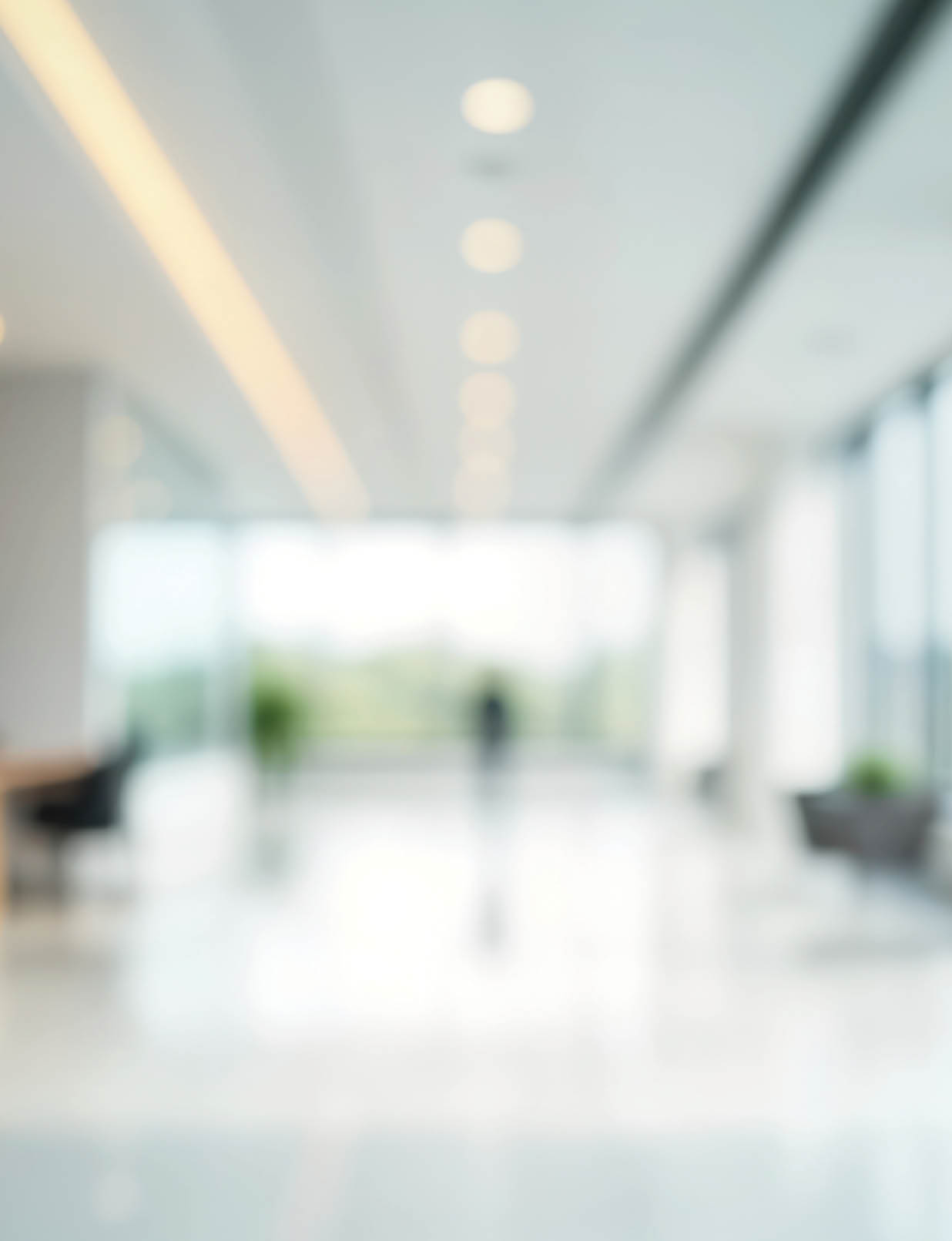 A bright, modern indoor space with large windows, ceiling lights, and a person standing in the distance. Description generated by AI