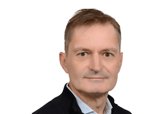 A person with short hair wearing a dark jacket over a light blue collared shirt is looking directly at the camera with a neutral expression against a white background. Description generated by AI