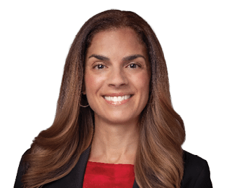 A person with long, wavy hair is smiling and wearing a black blazer over a red top against a white background. Description generated by AI